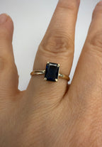 14k yellow gold emerald-cut sapphire ring on finger, dark blue stone side view