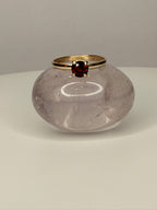 14k yellow gold ring with round dark red garnet center stone on display