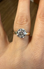 14k yellow gold moissanite ring featuring a round center stone, close-up finger shot