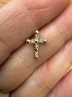 Gold cross pendant with diamond-set arms, close-up on fingers