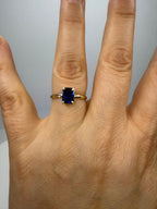 14k yellow gold emerald-cut sapphire ring on hand, dark blue square center stone